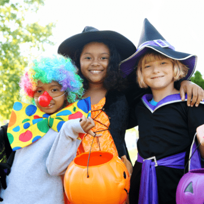 Photo of 3 children in costume. A clown and two witches with trick-or-treat buckets in the shape of jackolanterns