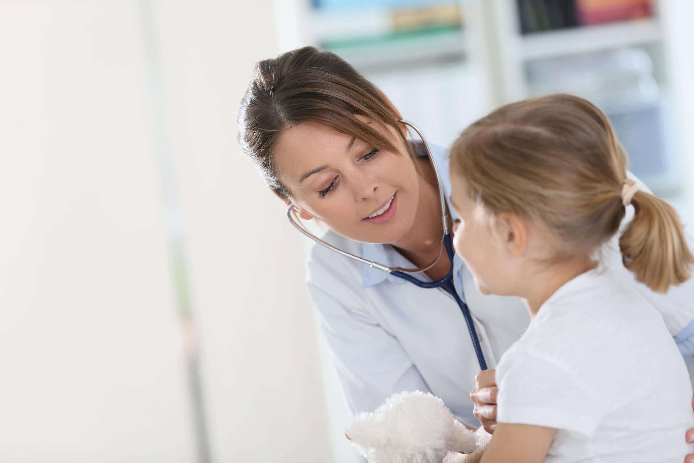 Pediatrician examining young girl with stethoscope.