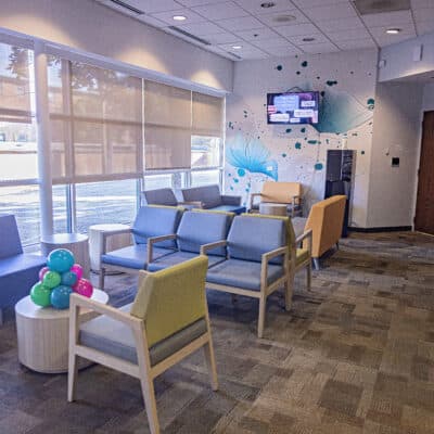 Lobby with ample seating in light colors. The far wall showcases a mural of a flower along with a tv display showing information