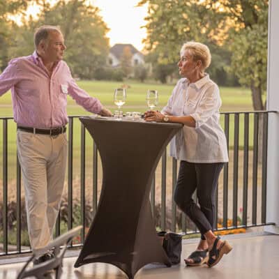 Two people stand at a tall table with golf course in background