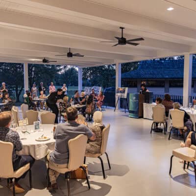 Veranda with tables of people looking to the right at Angela Curran at podium