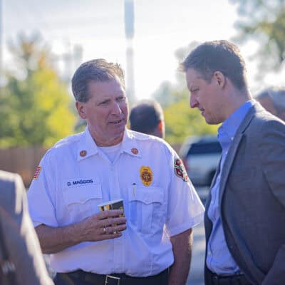 Two men stand talking to one another one in a suit coat the other in a police uniform