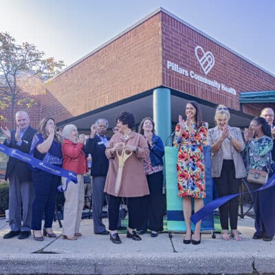 A group of people stand in front of a building, cutting a ribbon in motion