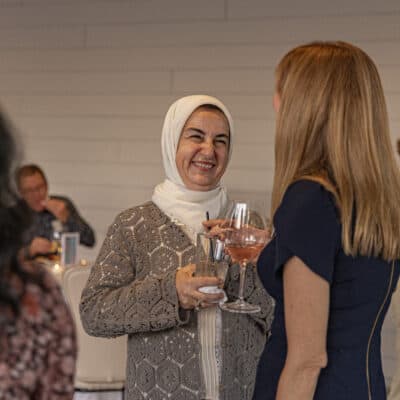 Woman wearing a headscarf speaks with woman holding a glass of wine