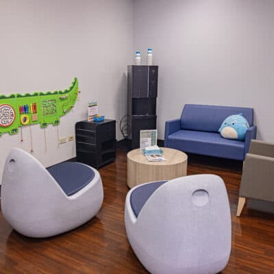 Behavioral Health waiting room with multiple seating options, a water cooler and a green alligator shaped children's activity toy attached to the wall