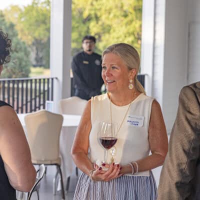 Woman stands with a glass of wine speaking to another woman