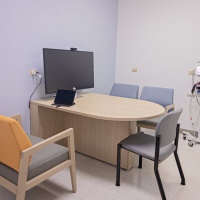 Telehealth suite with a table attached to the wall surrounded by 4 chairs and featuring a large screen.