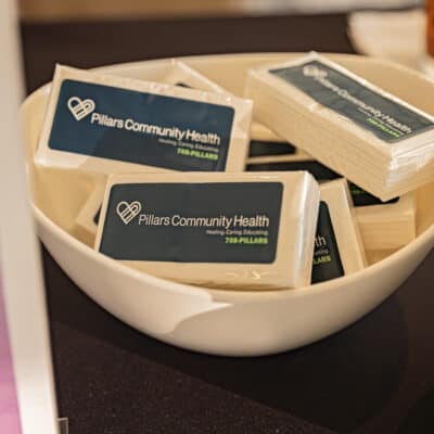 White ceramic bowl with tissue packs with a navy label featuring a white Pillars Community Health logo