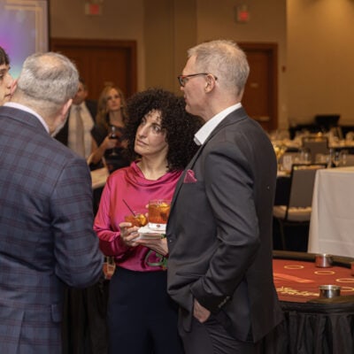Guests in formal attire gather and talk near a casino gaming table during the All In for PCH Gala