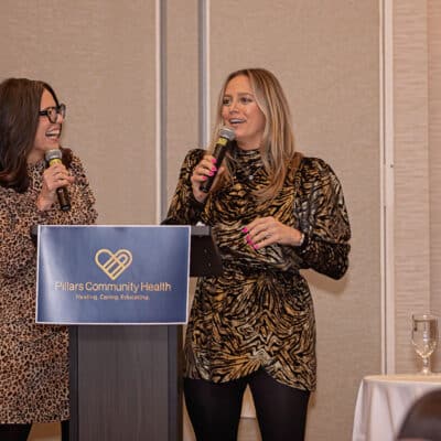 Lauren Ciancio and Michelle Anderson of The Sister Project speak together at the podium during the All In for PCH Gala.