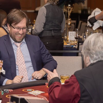 Guests sit at a blackjack table placing chips while a dealer manages the game during the All In for PCH Gala.