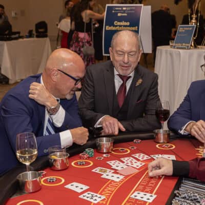 Guests gather around a blackjack table placing chips and reviewing cards during casino entertainment at the All In for PCH Gala.
