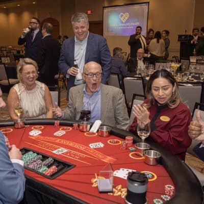 Guests react with excitement while playing cards at a casino table during the All In for PCH Gala.