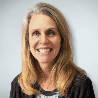 Professional headshot of Katherine "Kathy" Schilder smiling at the camera, wearing a black cardigan over a patterned top against a soft blue background.